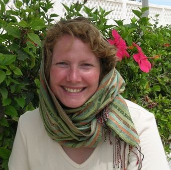 Jennifer Moore smiling wearing a green scarf beside a hibiscus hedge 