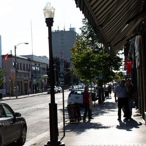 A view of a street in Downtown Peterborough. There are vintage-style streetlights and handing planters lining the sidewalk.
