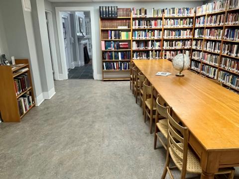 The College Library in Scott House. On the right side of the room are a long, wooden table with chairs and floor-to-ceiling bookcases. The left side of the room has a small bookshelf and a doorway into the Greg Piasetzki Reading Room.