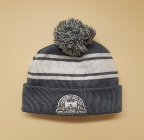 A grey knit hat with a white Traill College logo on the upturned brim. There are white stripes on the middle portion of the hat and a grey and white pompom on top.