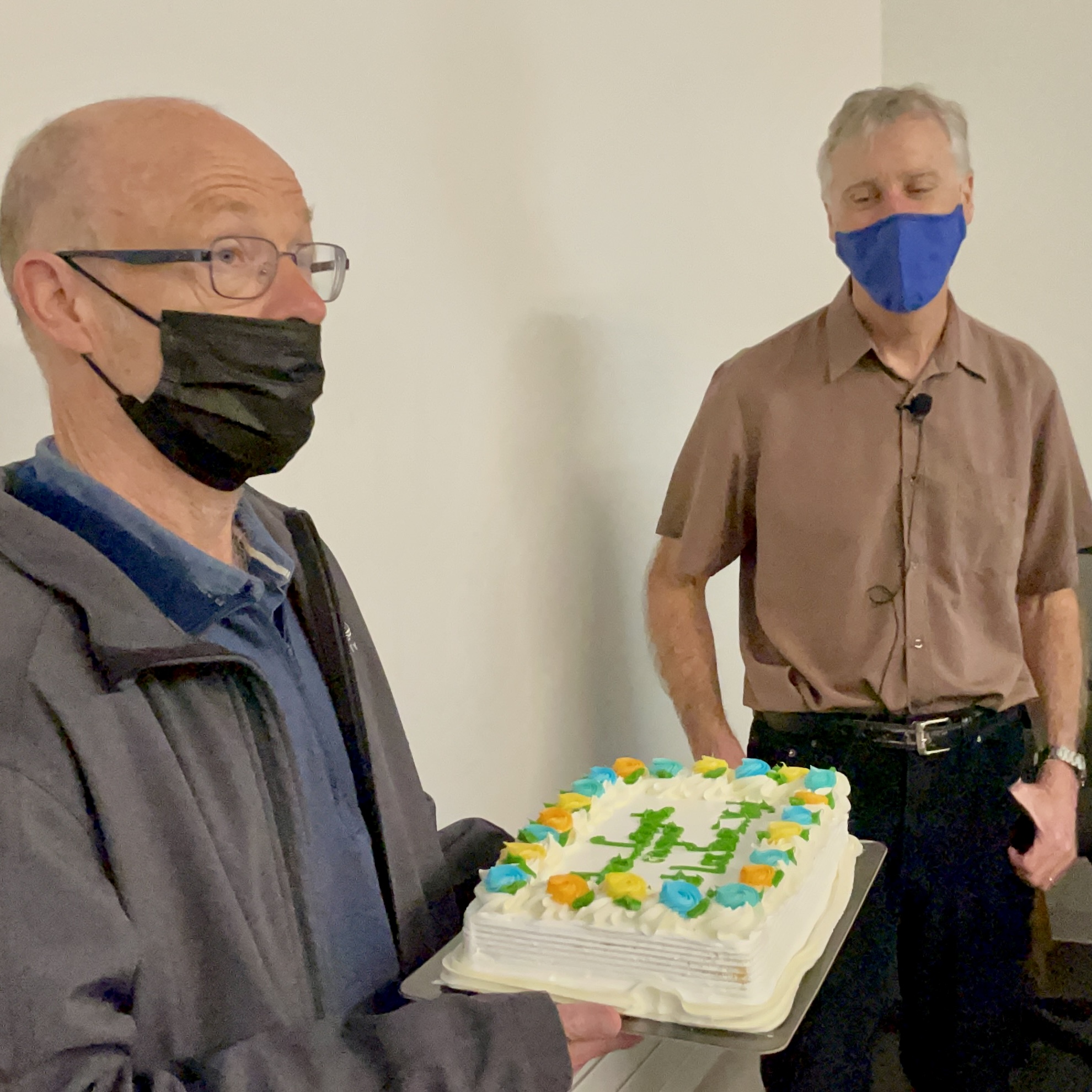 two white men in a classroom with a cake