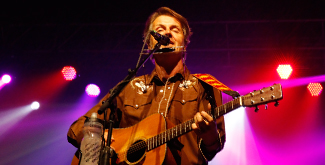 Band leader playing his guitar and harmonica on stage at the Blue Rodeo concert for Trent's 50th anniversary celebrations