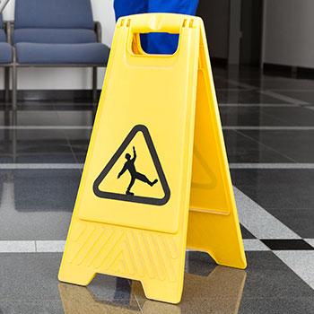 yellow hazard sign indicating a slippery floor is in front of a person who is mopping the floor.