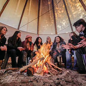 Students sitting in the tipi talking around a fire
