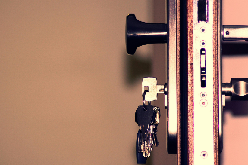 Close-up of a door latch with a set of keys inserted, set against a softly blurred background.