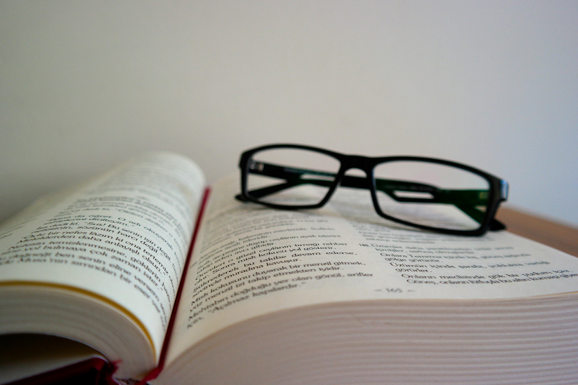 An open book with reading glasses resting on the pages, symbolizing focused study or research.