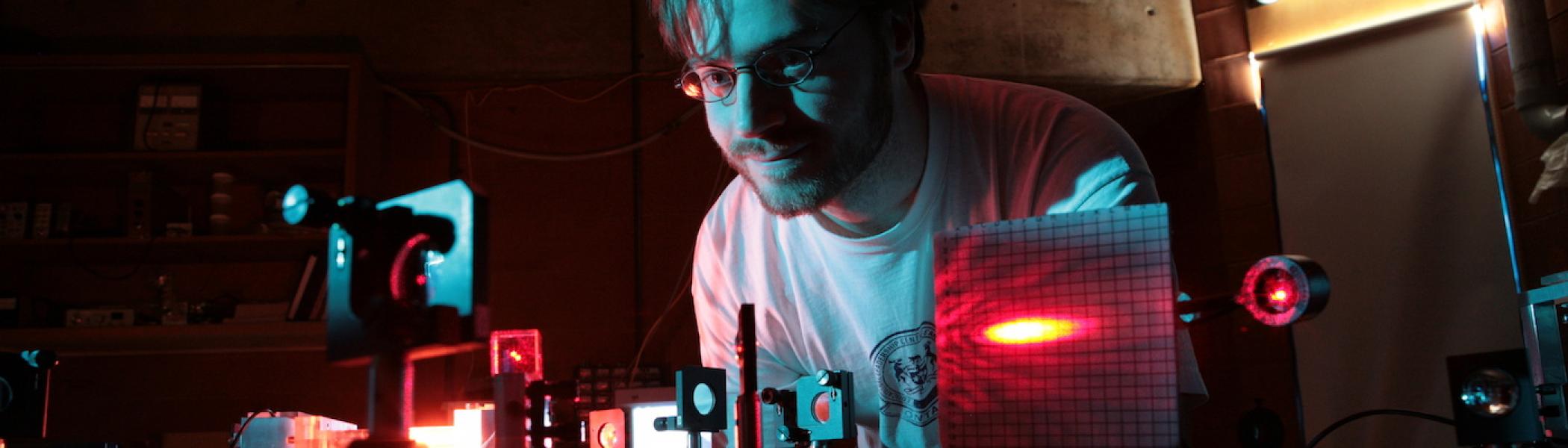 A student looking down at some electronics on his desk in dark red lighting