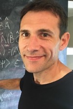 Carlo Bradac standing in front of a blackboard smiling