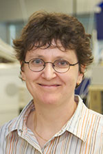 Lady with shorter, curly hair and glasses smiling at the camera whilst in the lab.