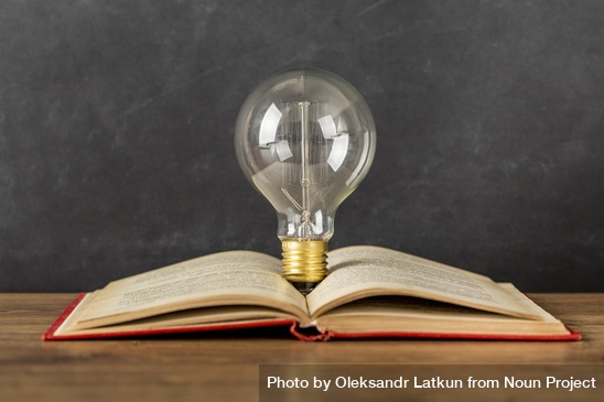 A lightbulb perched in the middle of an open book, on a table