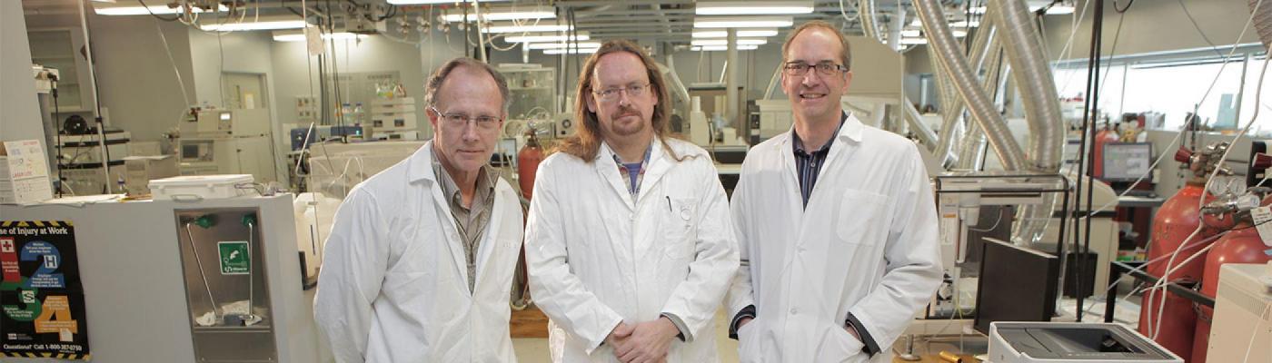 three individuals in white lab coats standing next to one another in the water quality centre