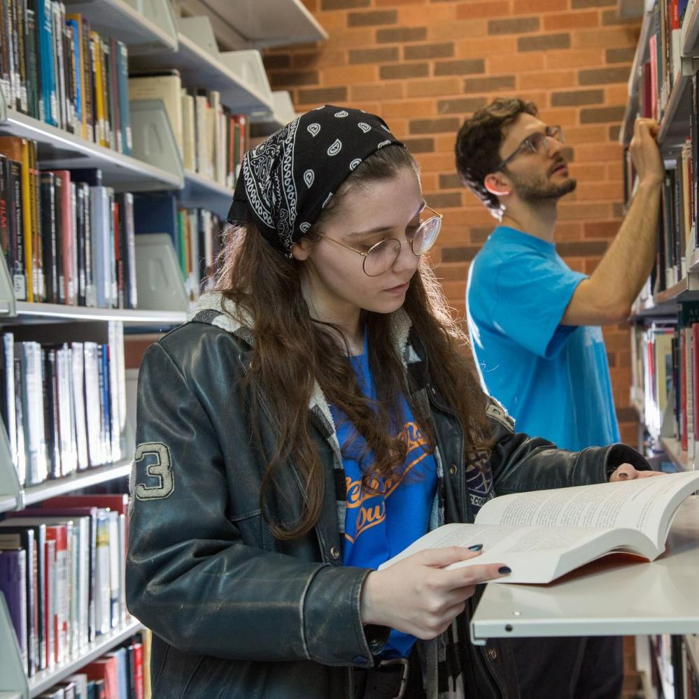 Two people looking at books in the library stacks.