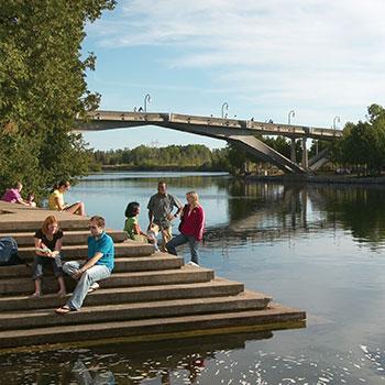 Students sitting on steps overlooking the Otonabee river on a summer day