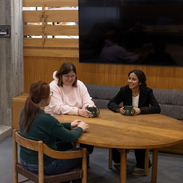 Two students and a staff member sitting at a round table, smiling