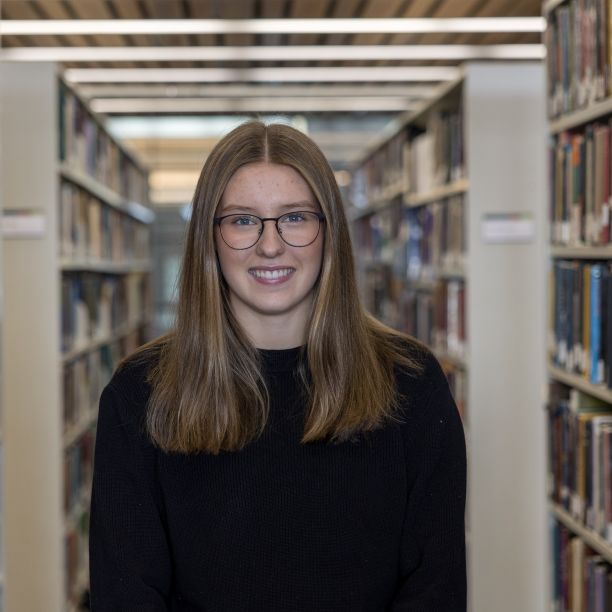 Emily, a transfer student, standing between stacks of books at Trent’s Bata Library 