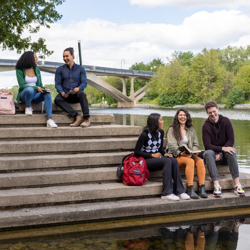 photo of five students sitting on stairs next to the Otonabee river