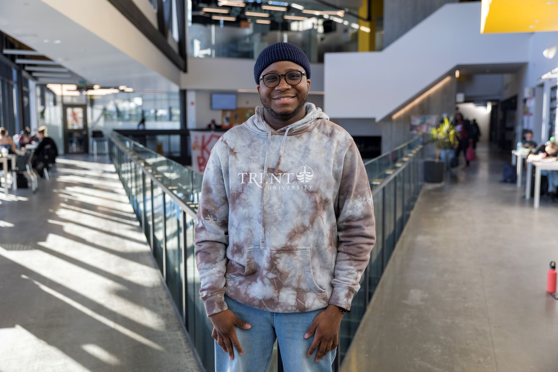 Student wearing a Trent hoodie, standing in the Student Centre and facing the camera, smiling