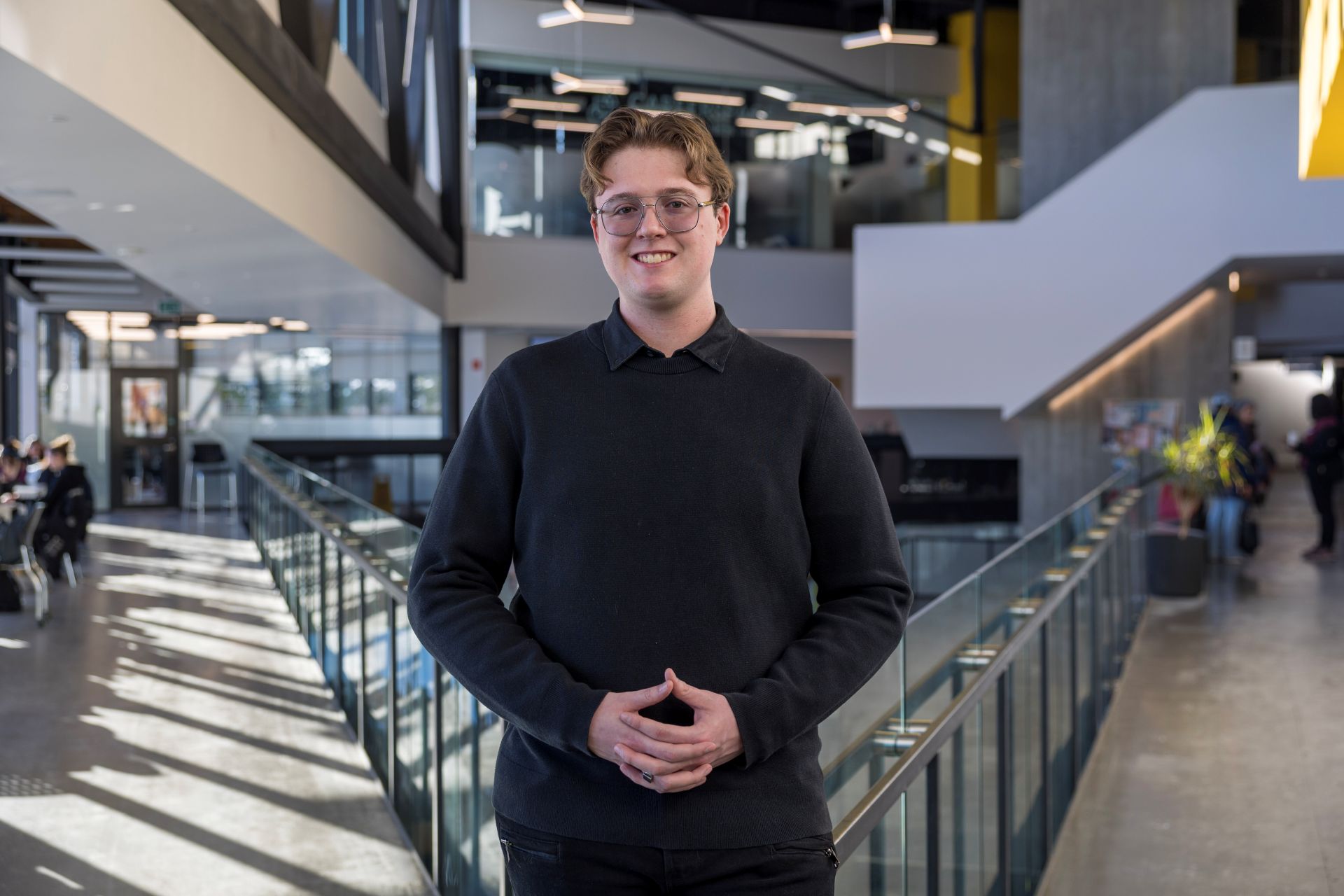 Student wearing black and standing in the Student Centre, smiling at the camera