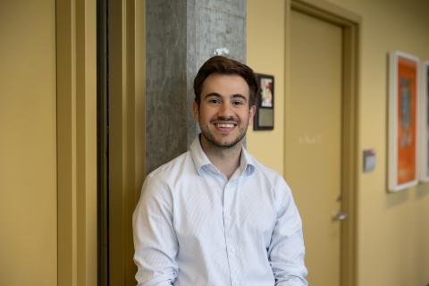 This is a photo of a man smiling again a pillar located on a yellow wall.