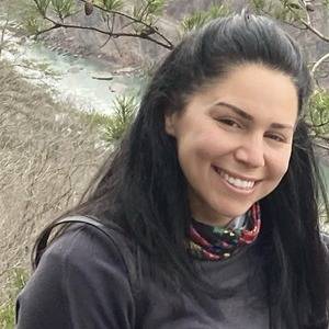 A photo of Heidi Burns. She is outdoors. Heidi has dark hair down to her shoulders and is smiling at the camera.