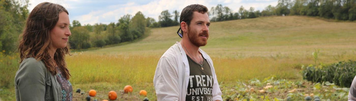 A male student standing in a field looking off into the distance in the autumn, with pumpins in the background