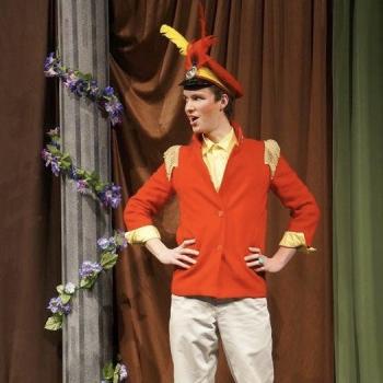 an actor on stage in a red coat and feathered hat