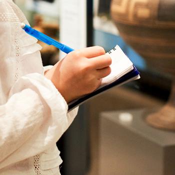 girl writes down notes while viewing museum exhibit