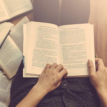 hands hold a book while 5 books are open on the ground around it