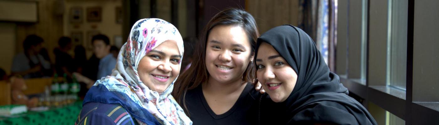 Three girls with two of them wearing a Hijab standing together and smiling