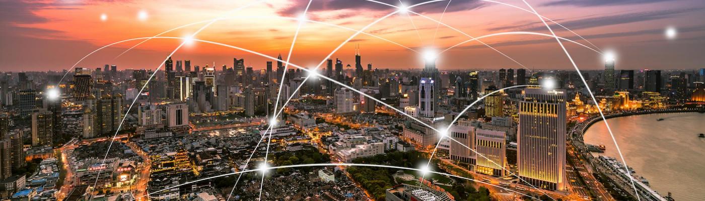 A city with a sunset in the background and lights going from one side of the city to the other