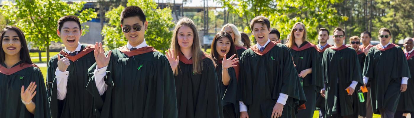 A line of graduating students on convocation day waving and smiling at the camera