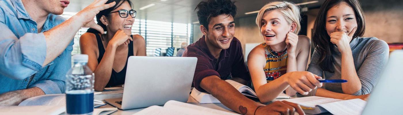 Five people sitting around some laptops and smiling