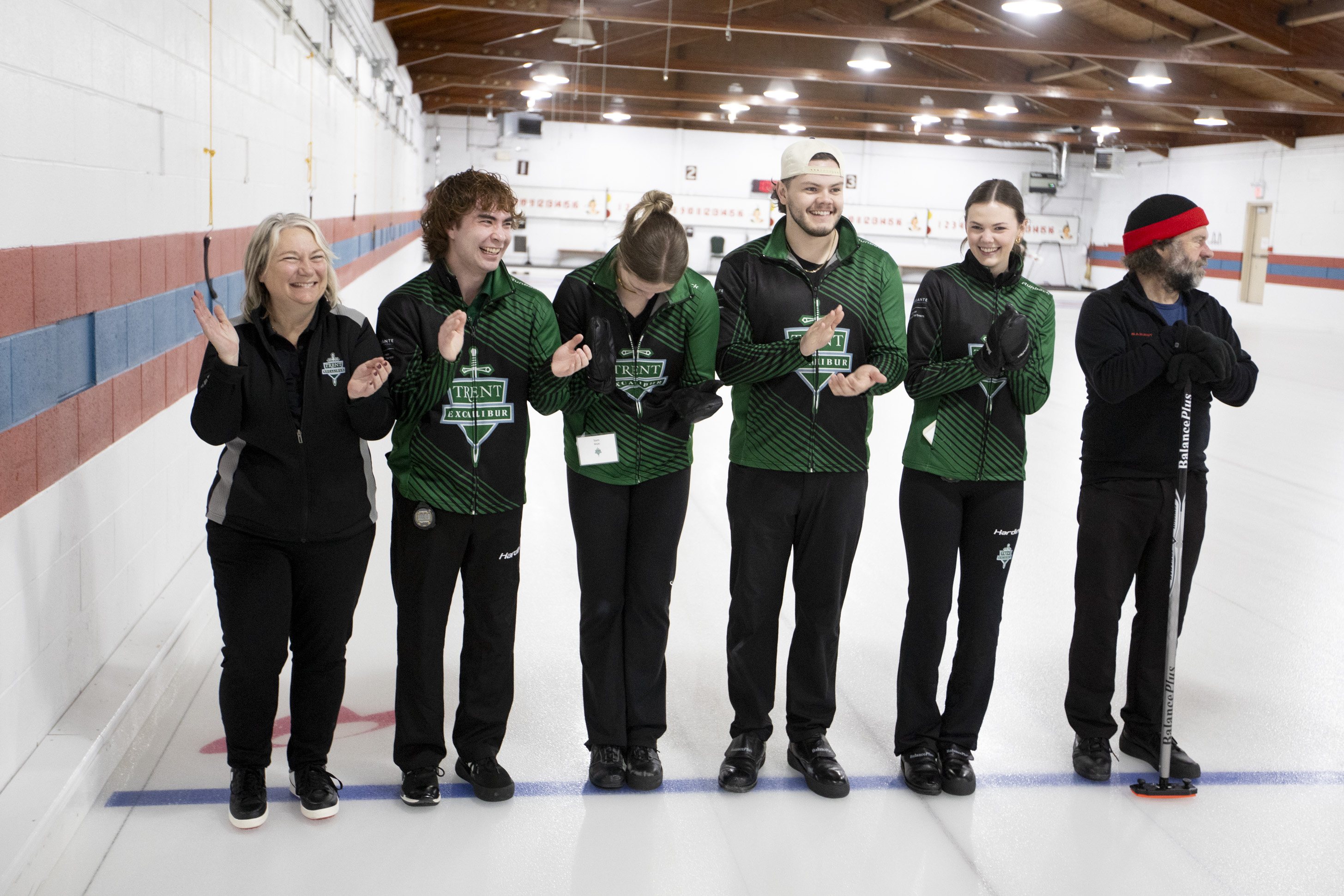 Six people standing in a line on curling ice surface