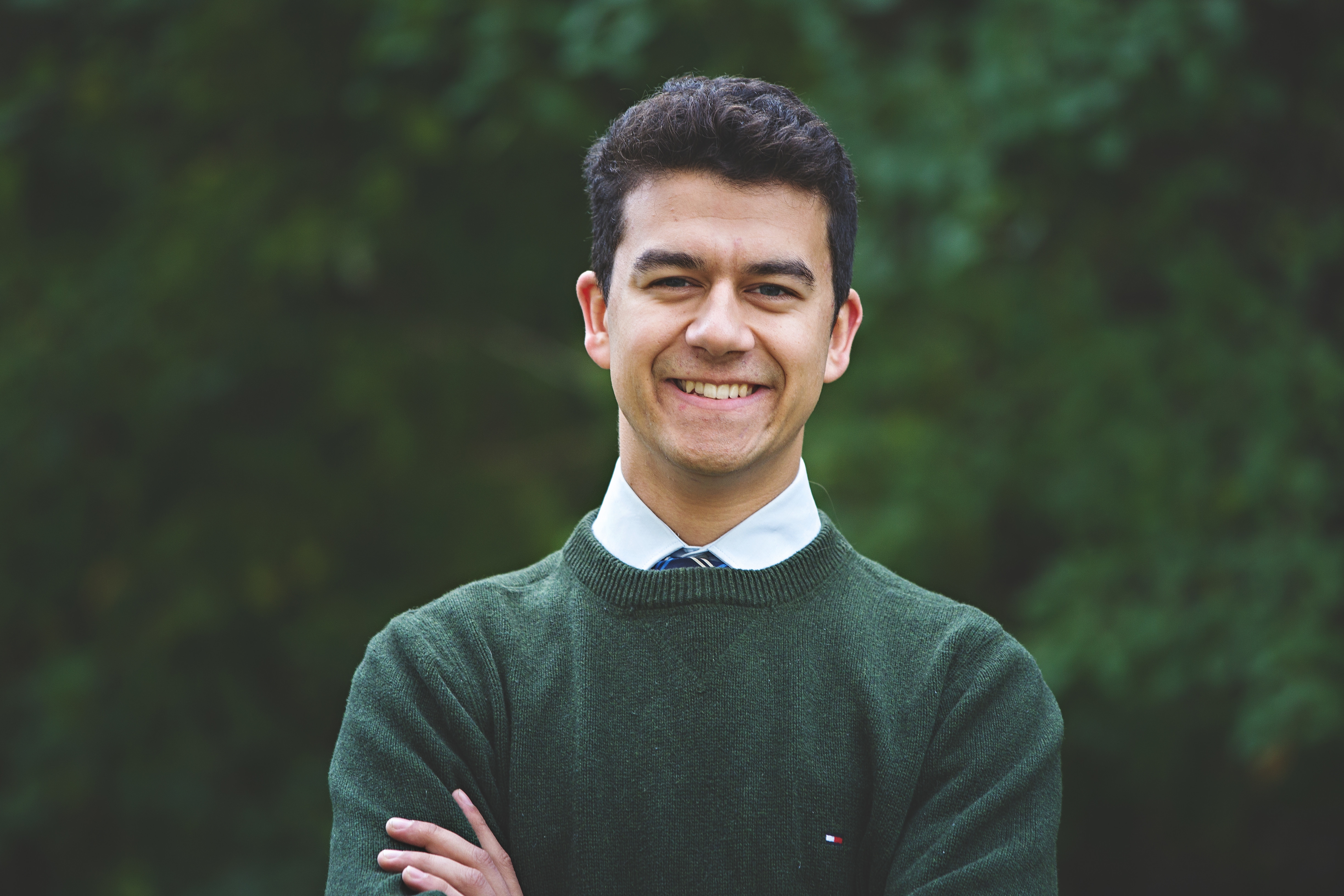 student in green sweater standing in front of green trees on Trent's Peterborough campus