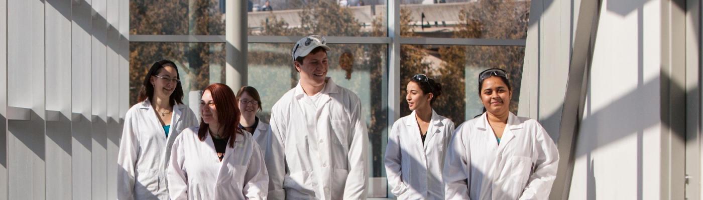 5 students walking along a hallway in white labcoats