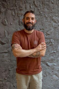bearded man standing with crossed arms in front of grey stone wall
