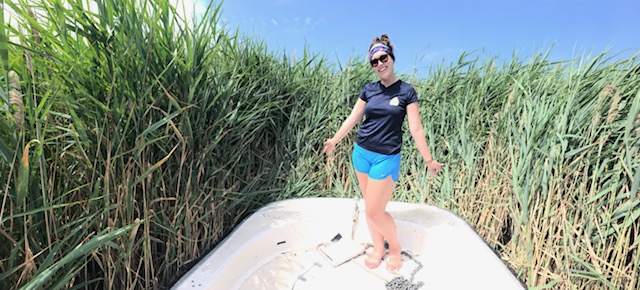 student, abby wynia, standing in tall grass posing and smiling at camera - doing research 