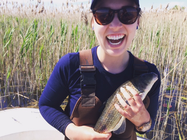 student, Abby Wynia, holding a fish with huge smile on her face wearing sunglasses