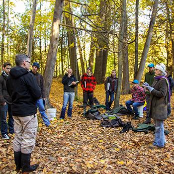 Dr. Michael Frost standing outside in the woods in the fall addressing a a group of students