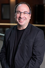 Man with black suit and glasses smiling at the camera