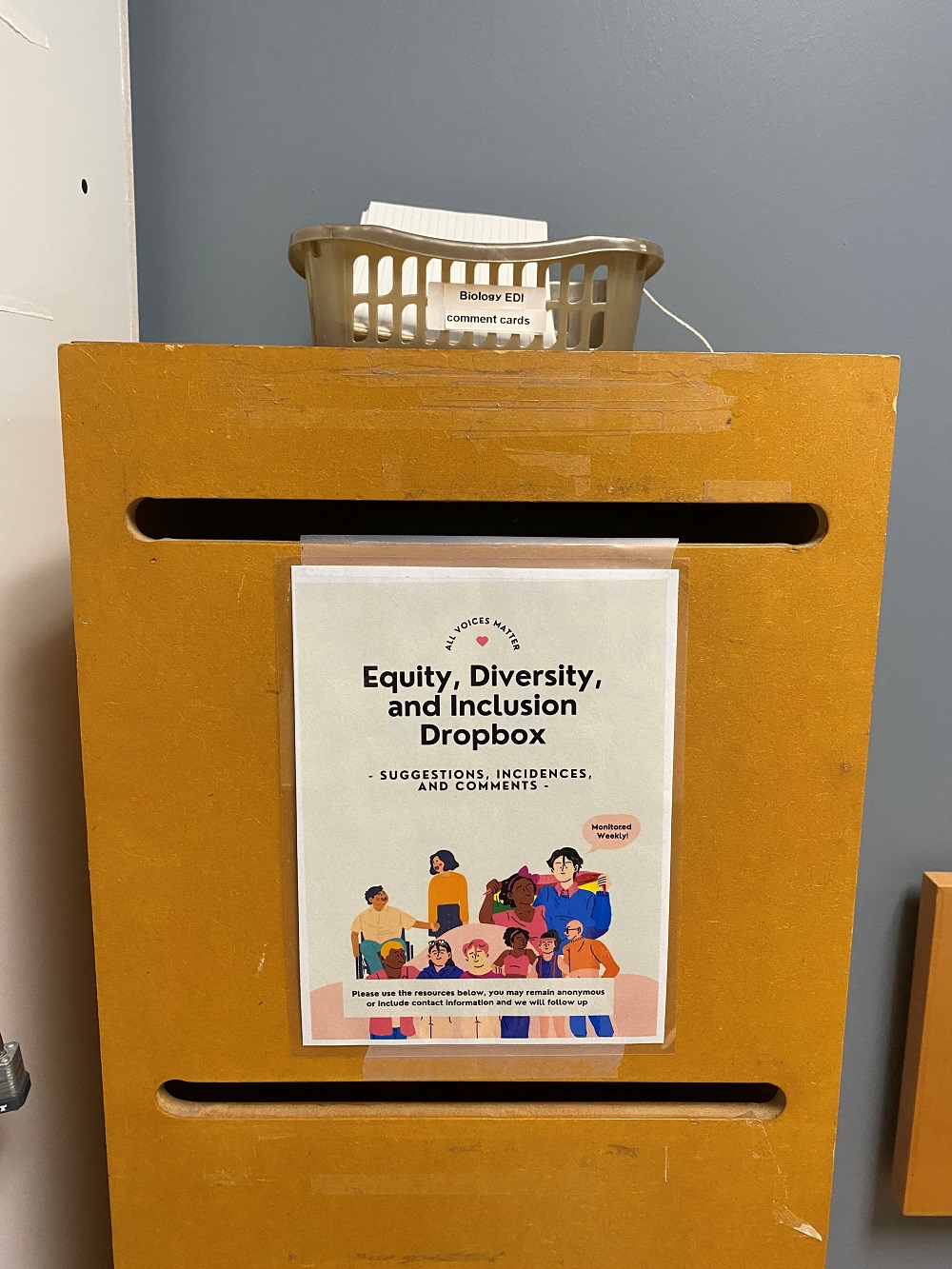 Wooden drop box with an equity, diversity and inclusion poster pasted on the front and box of comment cards on top