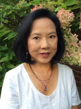 Janet Yee in front of a pink hydrangea bush wearing a white shirt and smiling at the camera.