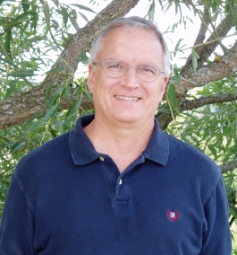 David Lasenby smiling at the camera in front of tree branches with leaves