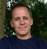 Jim Shaefer standing in front of trees wearing a navy blue shirt and smiling at the camera.