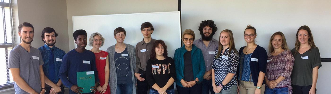 A group of people standing side by side in a line in front of a projector screen in a classroom