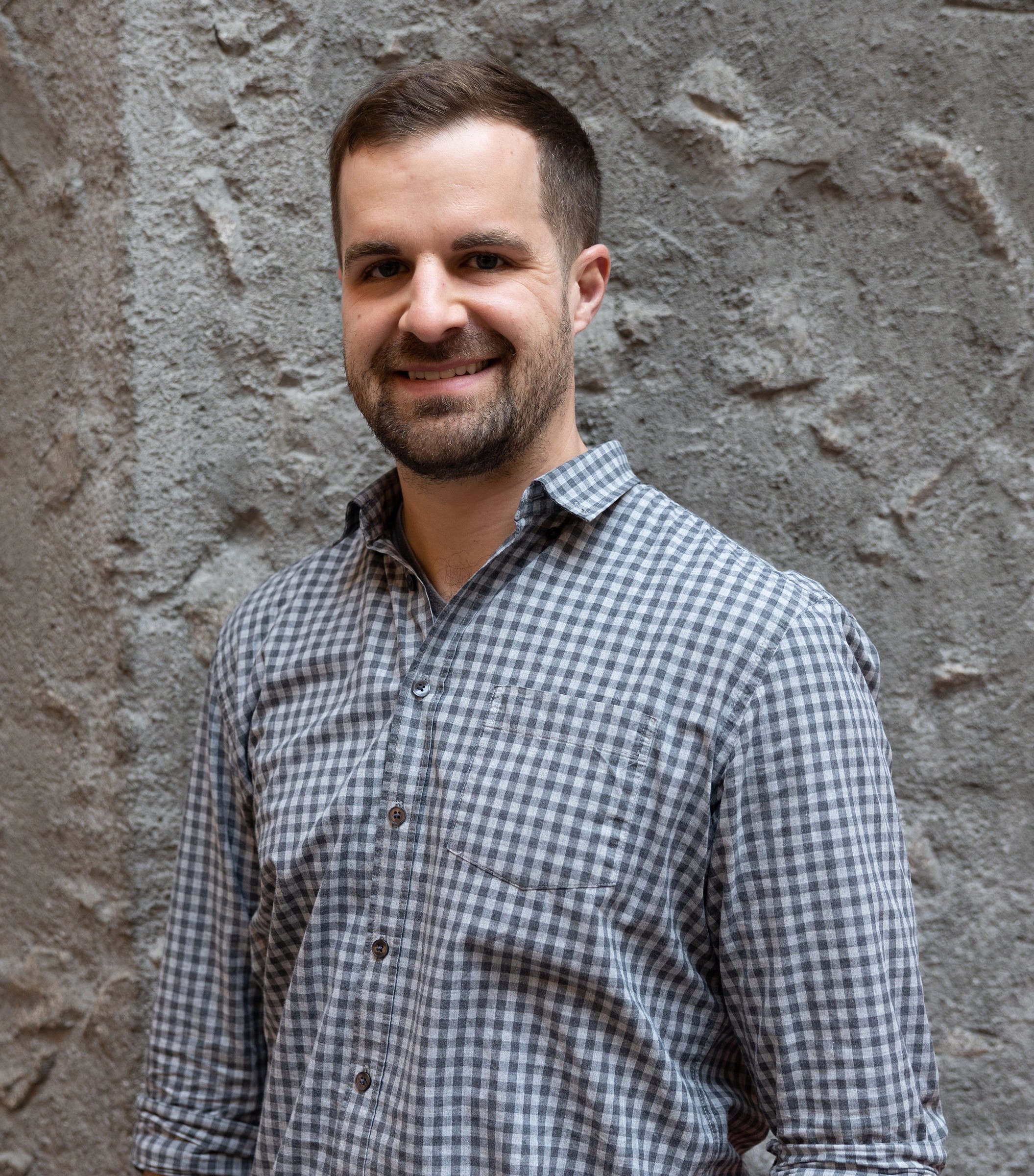 Dr. Graham Raby smiling in front of a grey rock wall