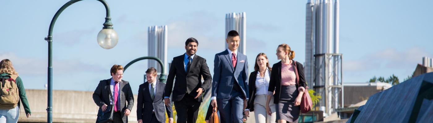 A group of students in business suits walking across the Faryon bridge in the afternoon fall sun