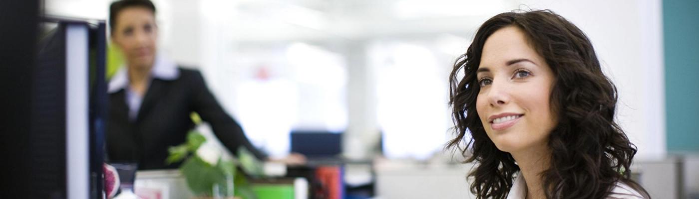 A woman with long brown hair smiling while sitting at her office desk in the daylight