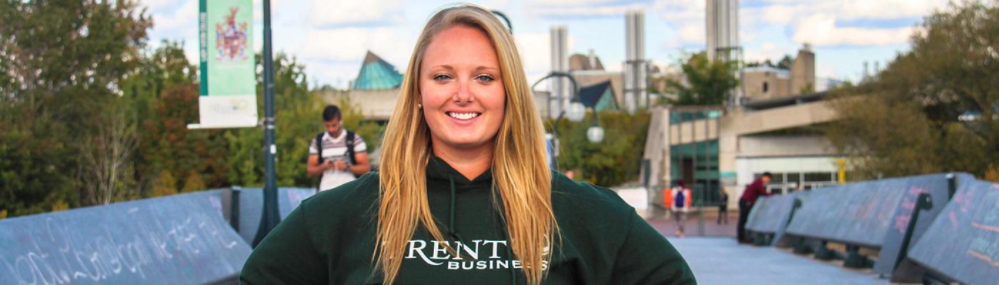 Female student standing on the Faryon bridge on a summer's evening in her Trent Business green hoodie