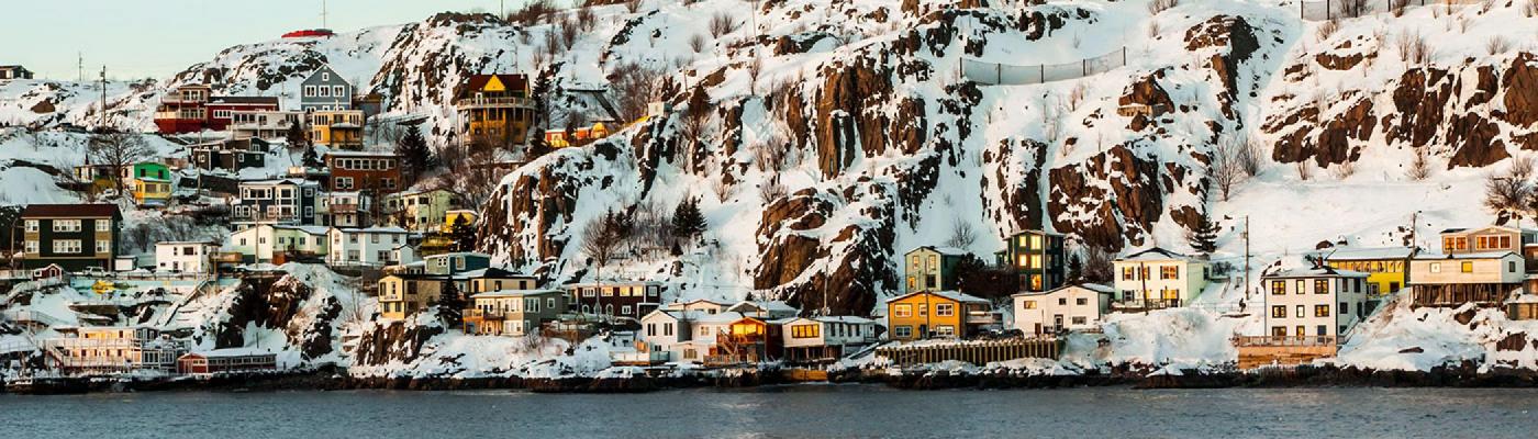 A town of colourful houses set next to water and a snowy rockface 